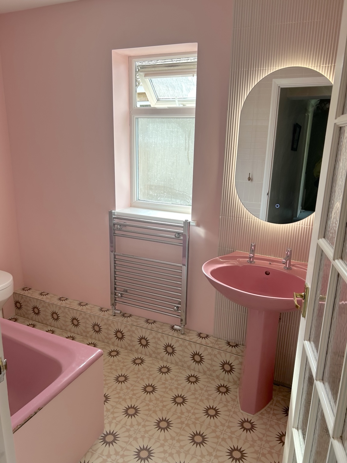 The finished pink bathroom — basin, illuminated mirror, radiator, patterned floor and pink bath